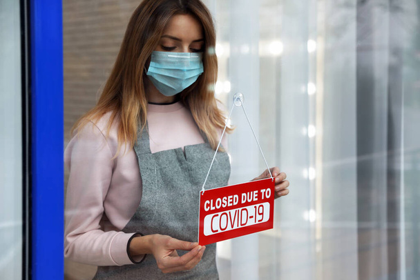 Propriétaire d'entreprise en masque suspendu panneau rouge avec texte fermé en raison de Covid-19 sur porte en verre. Quarantaine de coronavirus - Photo, image