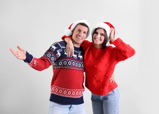 Beautiful happy couple in Santa hats and Christmas sweaters having fun on light background - Фото, зображення