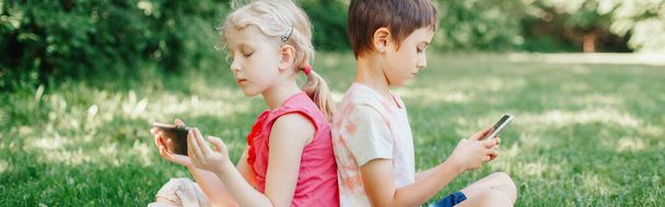 Poika ja tyttö lapset pelata pelejä älypuhelimissa ulkona. Lapset digitaalinen gadget näytön riippuvuus. Nykyajan yksinäisyyden ongelma yhdessä. Web-bannerin otsikko. - Valokuva, kuva