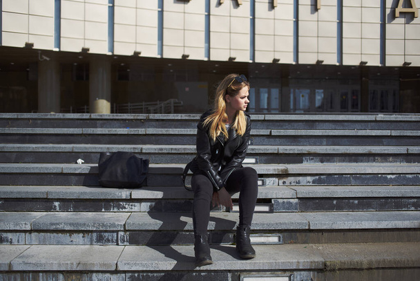 Una donna in giacca di pelle siede sulle scale vicino al teatro sul modello di strada - Foto, immagini