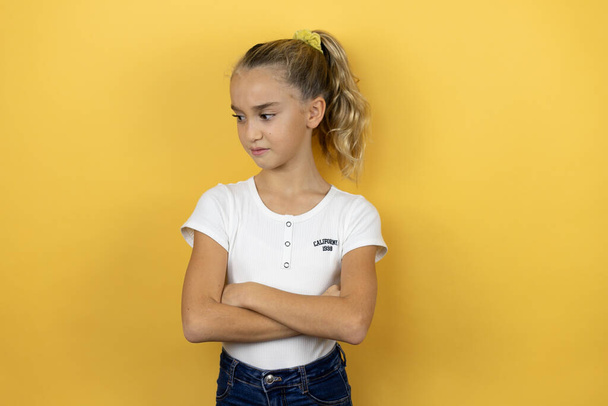 Nuori kaunis lapsi tyttö seisoo yli eristetty keltainen tausta ajattelu näyttää väsynyt ja kyllästynyt ristissä kädet - Valokuva, kuva