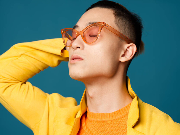A man in orange glasses holds his hand behind his head and an orange jacket - Foto, Imagem