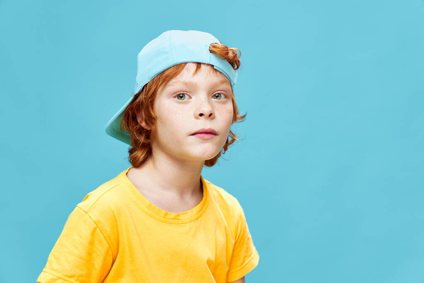 Περίεργο κοκκινομάλλικο αγόρι με μπλε καπέλο στο κεφάλι του που κοιτάει μπροστά με κίτρινο μπλουζάκι  - Φωτογραφία, εικόνα