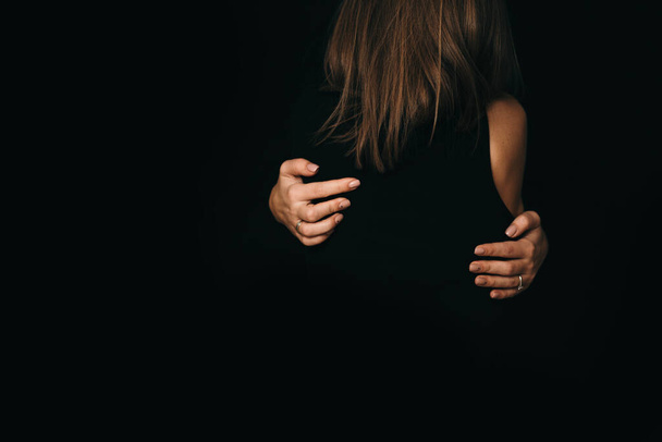 The girl hugs her back. Depression in modern man. The girl stands with her back against a black background - Photo, Image