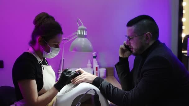 Ein Mann lässt sich im Nagelstudio die Nägel machen - Meister schiebt seine Nagelhaut mit einem Drücker - Filmmaterial, Video