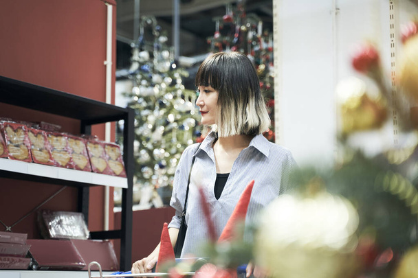 倉庫店でショッピングカートを押すアジアの女性クリスマスの装飾&ギフトを購入 - 写真・画像