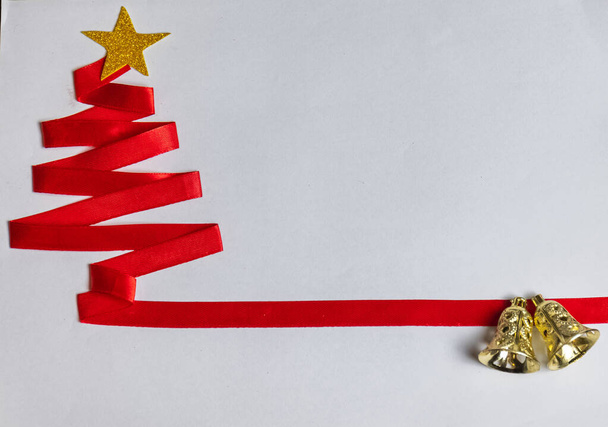 Κόκκινο χριστουγεννιάτικο δέντρο φτιαγμένο με κόκκινη κορδέλα και χρυσό αστέρι και χριστουγεννιάτικες καμπάνες σε λευκό φόντο. - Φωτογραφία, εικόνα