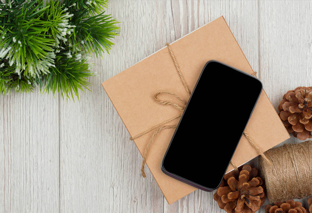 クリスマスオンラインショッピング。モックアップ、クリスマスと新年のコンセプトの木製の背景に空白の画面スマートフォン、フラットレイ。トップビュー、コピースペース . - 写真・画像