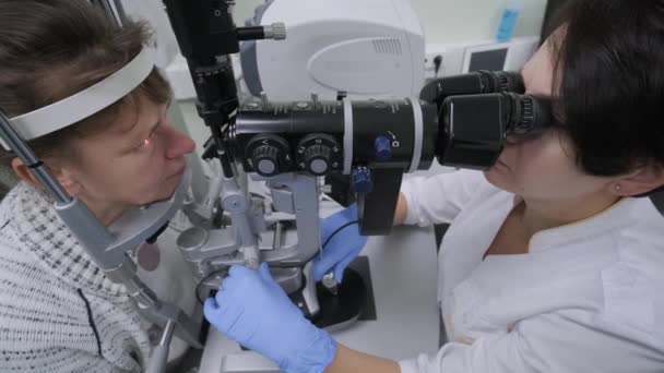 La doctora está viendo a través del oftalmoscopio en los ojos de la paciente en la clínica oftalmológica. Inspección profesional de la visión - Imágenes, Vídeo