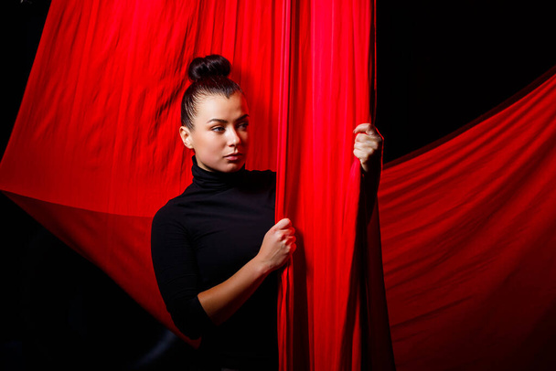 Portrait of a sports girl on a background of red cloths for aerial gymnastics. Studio shooting on a dark background, - Foto, imagen