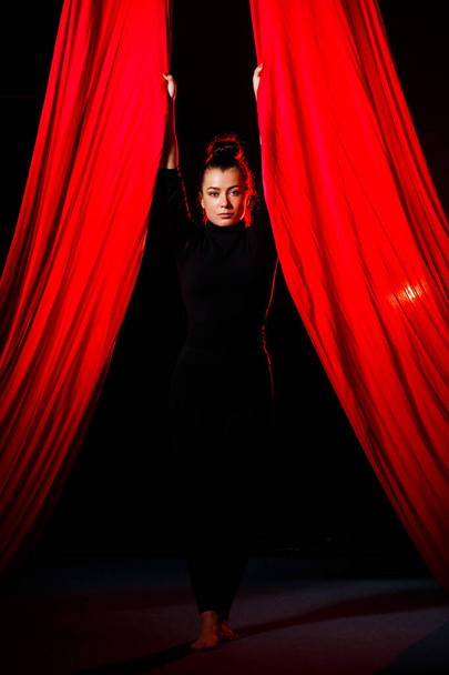 Una donna è impegnata in acrobazie aeree su uno sfondo scuro. Ginnasta sportiva che fa esercizi su tela - Foto, immagini