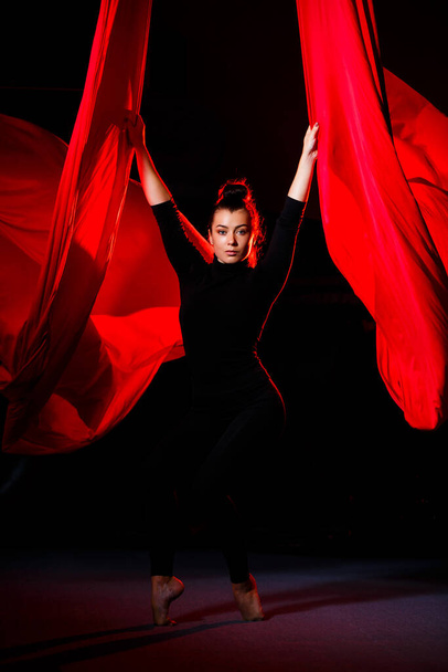 Красивая спортивная девушка-акробатка выполняет гимнастические и цирковые упражнения на красном шелке. Спортивная гимнастика на холсте - Фото, изображение