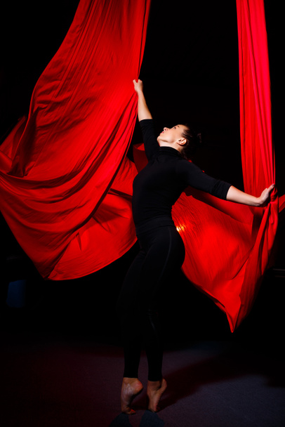 Eine schöne sportliche Akrobatin führt Turn- und Zirkusübungen auf roter Seide aus. Luftturnen auf Leinwand - Foto, Bild