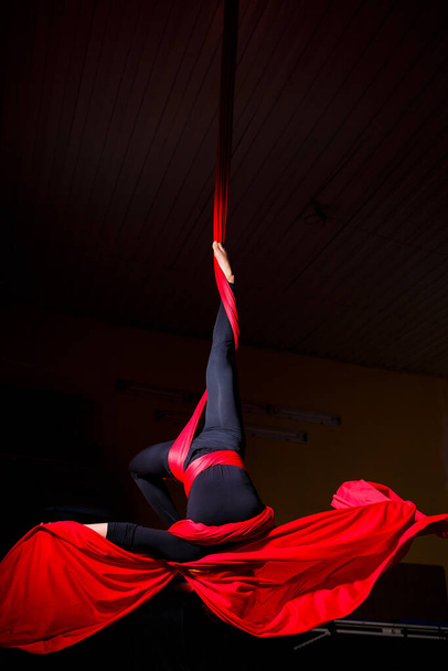 Portrait d'un beau acrobate sur toile sur fond sombre. Elle fait des ficelles. Gymnaste aérien - Photo, image