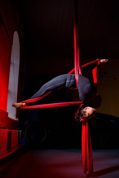 Portrait of a beautiful acrobat on canvas against a dark background. She does twine. Aerial gymnast - Photo, Image