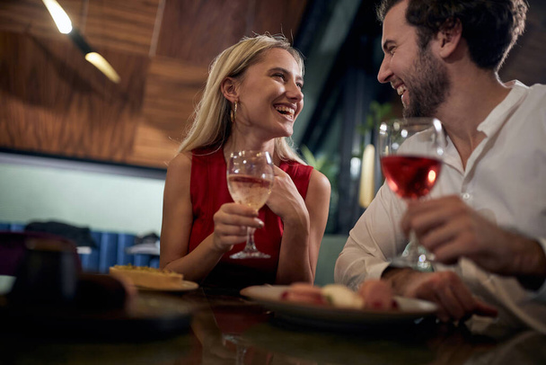 young couple looking each other, smiling, laughing,  having romantic dinner in a restaurant, celebrating new year.  - Foto, Imagen
