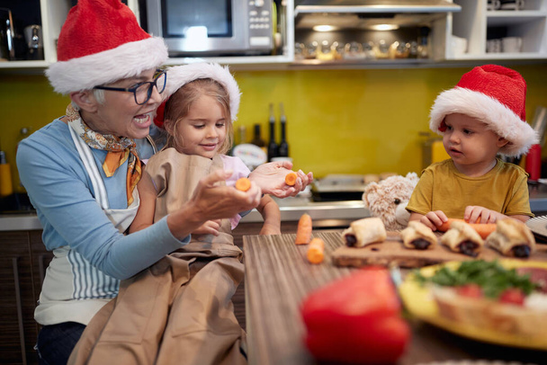 Grandma and grandchildren preparing Xmas meal in the kitchen in cheerful atmosphere together. Christmas, family, together - 写真・画像