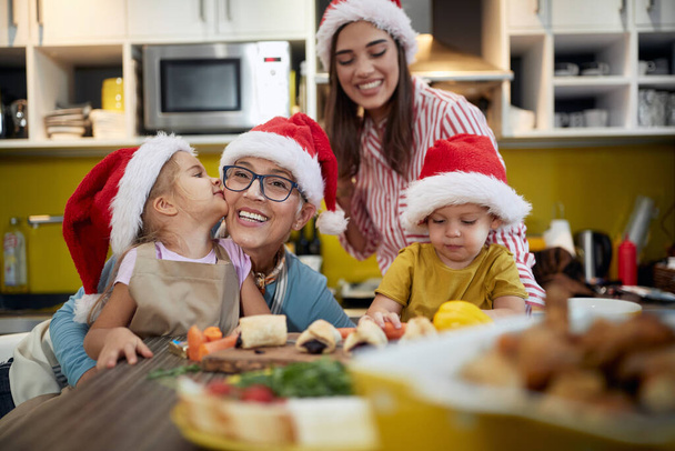 Children love spending time with grandma and mother in a festive atmosphere in the kitchen on Xmas. Christmas, family, together - Foto, afbeelding