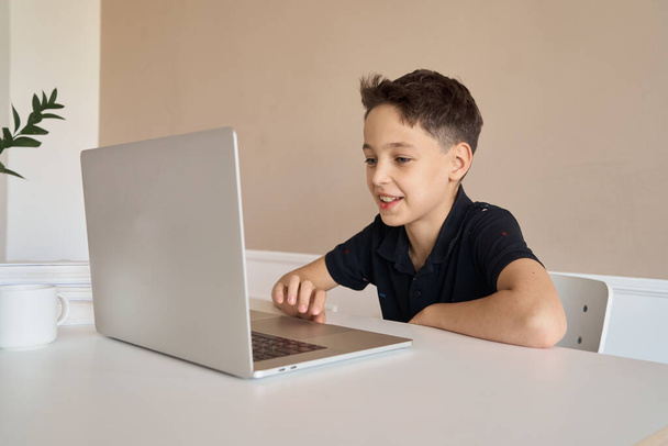 Schoolboy boy sitting at a desk with a laptop, writes school lessons during homework. - Foto, Imagem