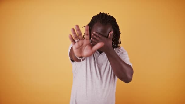 Schüchterner afrikanisch-amerikanischer Mann versteckt sich mit ausgestreckter Hand und anderem über dem Gesicht vor der Kamera - Filmmaterial, Video