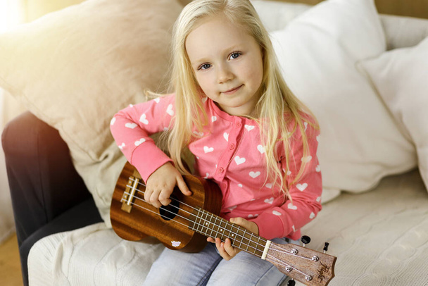 Little cute baby playing ukulele guitarin sunny room. Childhood concept - Foto, Imagem