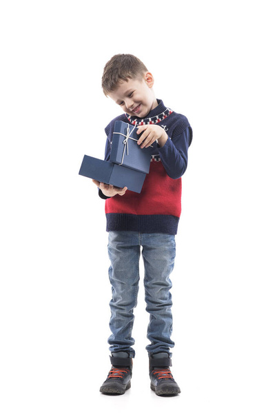 Smiling happy little kid in Christmas sweater holding opened gift box. Full body portrait isolated on white background.  - 写真・画像