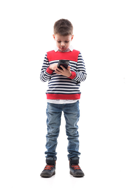 Cute little stylish kid using smart phone playing games or using apps with touch screen. Full body portrait isolated on white background.  - Foto, Bild