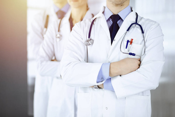 Group of modern doctors standing as a team with crossed arms and stethoscopes in a sunny hospital office. Physicians ready to examine and help patients. Medical help, insurance in health care, best - Фото, изображение