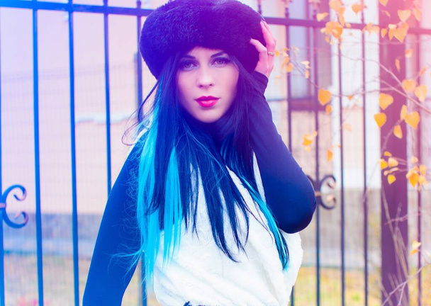 Retrato al aire libre de una joven hermosa mujer de moda posando en la calle. Modelo con boina negra y paño de piel de punto con pelo azul. Concepto de moda femenina - Foto, imagen