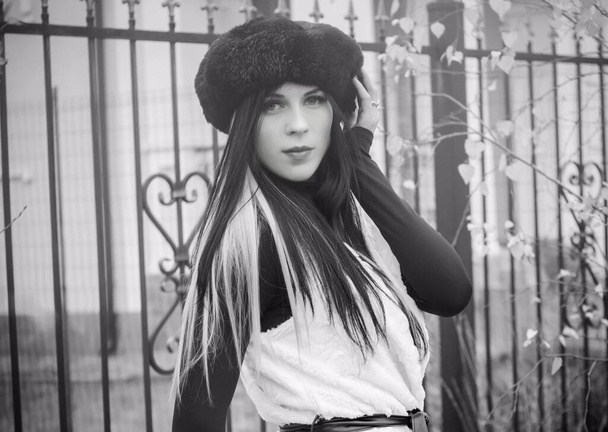Szabadtéri portré fiatal, gyönyörű, divatos nőről, aki az utcán pózol. Fekete svájcisapkát és kék hajú kötött szőrmeszövetet viselő modell. A női divat fogalma - Fotó, kép
