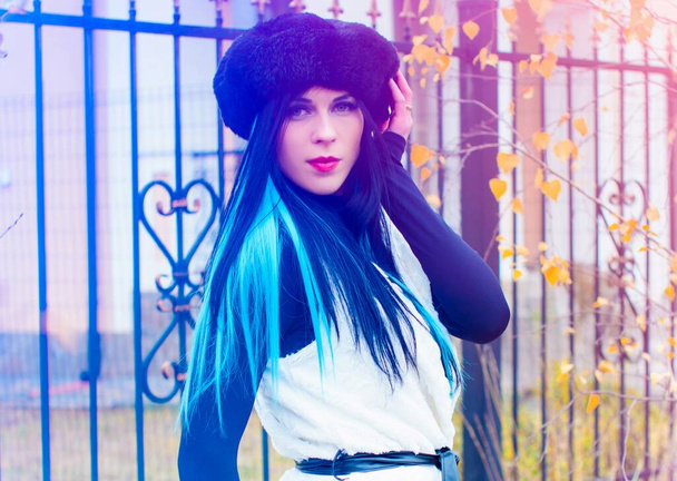 Ulkona muotokuva nuori kaunis muodikas nainen poseeraa kadulla. Malli yllään musta baskeri ja neulottu turkis kankaalla siniset hiukset. Naisten muoti käsite - Valokuva, kuva