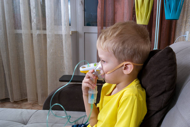 a 5-7 year old boy in a t-shirt takes an inhalation at home - Photo, Image