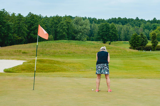 Close up portrait of woman standing with golf club outdoors. Female golf player wearing sportswear swinging on green field. - Fotografie, Obrázek