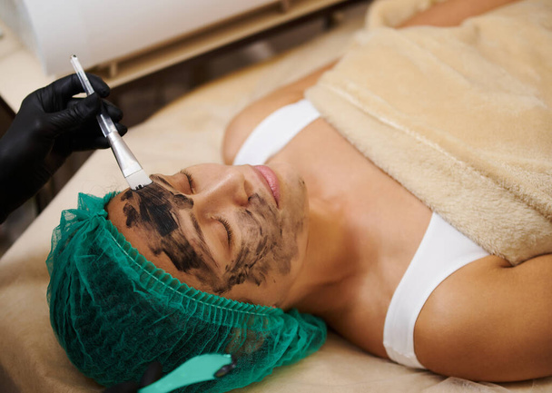 A fekete faszén kozmetikai maszkot a beteg arcára mossa - Fotó, kép
