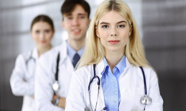 Group of three young doctors standing as a team with arms crossed in modern clinic and ready to help patients. Medicine concept - Fotografie, Obrázek