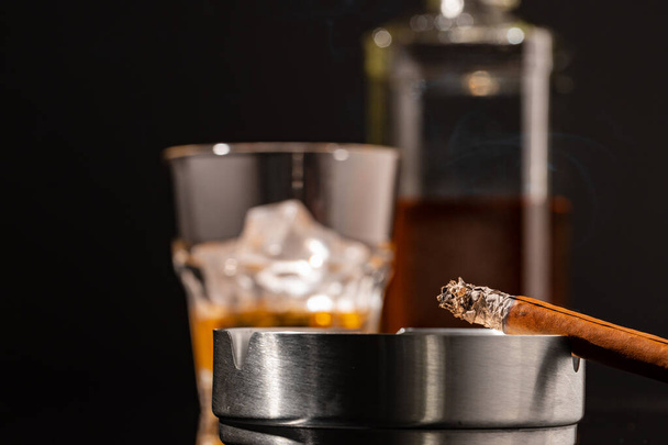 Glass of whisky and lighted cigar on black background - Фото, изображение
