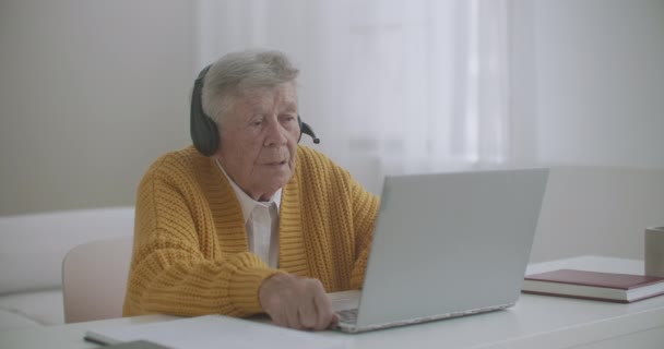 Az idős nő laptoppal telefonál, gesztikulál, és hüvelykujját felfelé mutató kézmozdulatot mutat. Az idős nő és a modern eszközök koncepciója. - Felvétel, videó