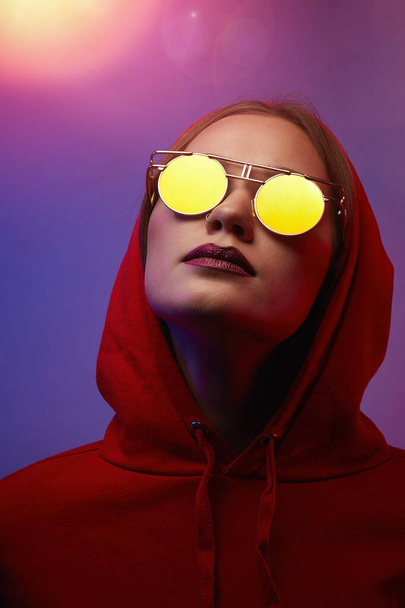 Fashion young woman model wear hoodie and eyewear sunglasses in neon light studio background. Close up. - Foto, Imagem