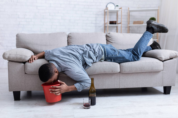 Hombre borracho vomitando en cubo después de beber vino acostado en el interior - Foto, imagen