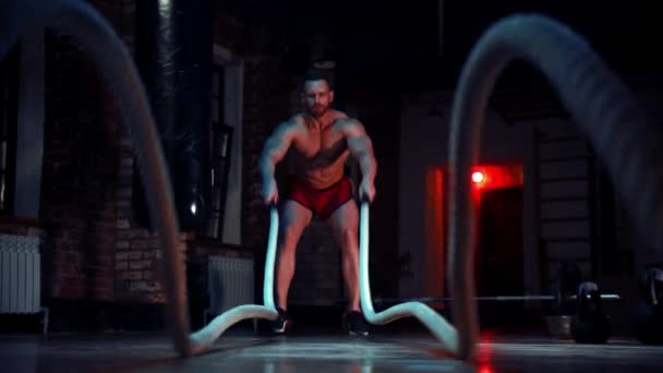 Σκληρός άνθρωπος στέκεται στο γυμναστήριο και κάνει ασκήσεις σχοινιών μάχης - Πλάνα, βίντεο