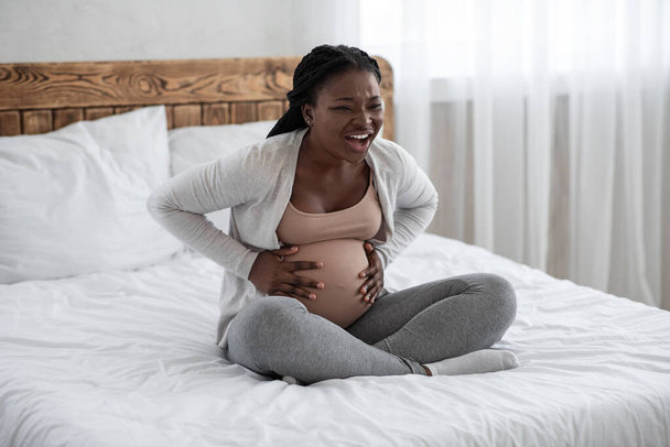 Embarazada negra teniendo contracciones de parto en casa, sufriendo de dolor de vientre - Foto, imagen