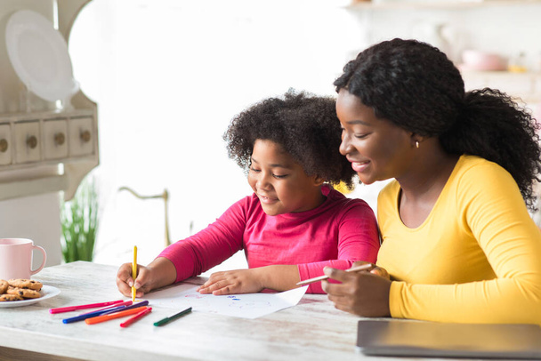 feliz negro madre y lindo poco hija dibujo juntos en cocina mesa - Foto, imagen
