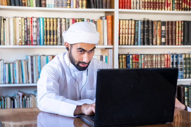 Arabe gars assis dans la bibliothèque universitaire écouter de la musique à l'aide d'écouteurs - Photo, image