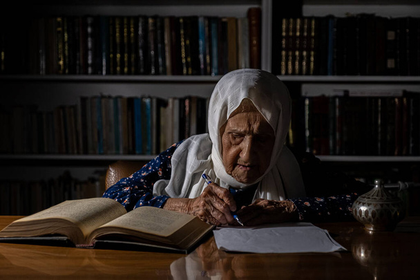 Γριά κυρία γράφει και διαβάζει κάποιο βιβλίο στο φως του πρωινού - Φωτογραφία, εικόνα