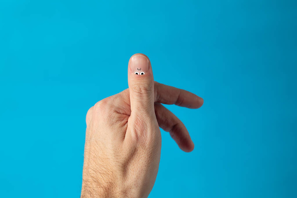 創造的なコンセプト、男性の爪、目と指で。青い背景で - 写真・画像