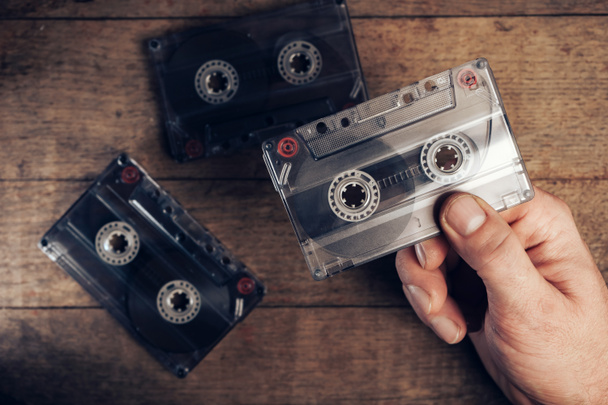 Hand vasthouden audio cassette tape op bruine oude houten tafel. Minimalisme retro stijl concept. Achtergrondpatroon voor ontwerp.  - Foto, afbeelding