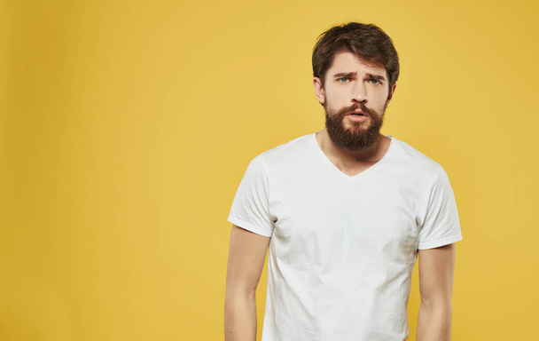 emotioneel bebaarde man in wit t-shirt studio gele achtergrond - Foto, afbeelding