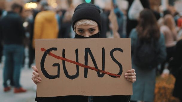 Silah yok. Yüzü maskeli genç bir kadın silahlı şiddete karşı pankart tutuyor. Gösteri ve devrim kavramı - Fotoğraf, Görsel