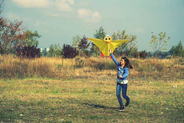 Nastolatka puszczająca żółty latawiec. Piękna młoda dziewczyna latawiec mucha. Szczęśliwa dziewczynka biegnie z latawcem w rękach na pięknym polu. stonowana. - Zdjęcie, obraz