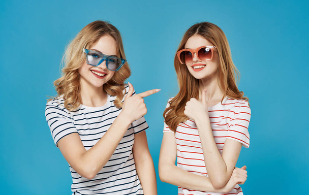 Leuke vriendinnen in gestreepte T-shirts donkere bril mode communicatie blauwe achtergrond - Foto, afbeelding